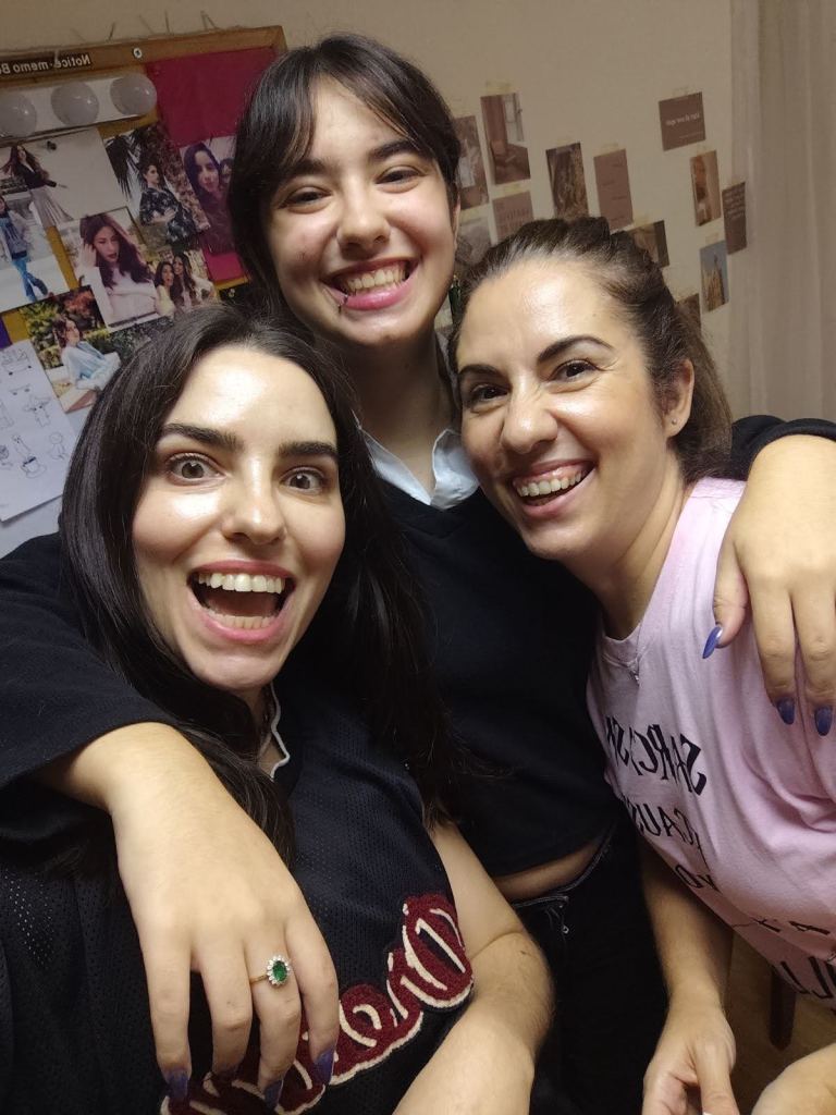 Τρεις γυναίκες χαμογελούν σε selfie, συνθέτοντας μια ευχάριστη οικογενειακή ατμόσφαιρα.